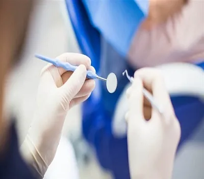 Gloved hands holding a dental mirror and explorer during an exam